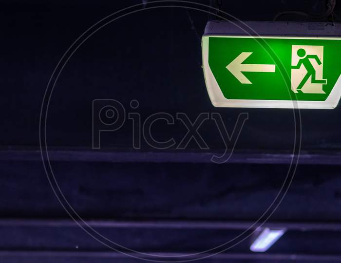 Green exit sign with running person and green arrow shows guidance system signage in a parking lot for rescue and evacuation safety in dangerous situations at ceiling to safe life in extreme danger