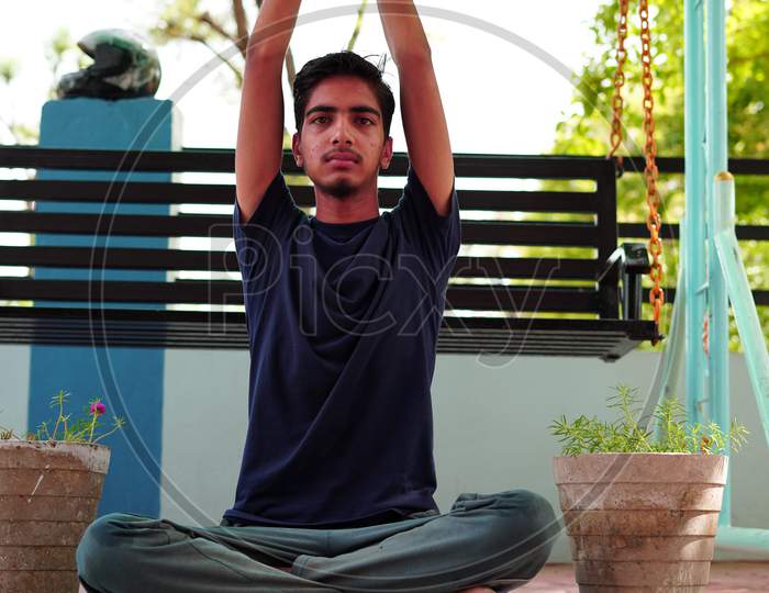 A Boy Is Meditating At Home In India. Indian Young Boy In A Black Traditional Shirt Sitting In A Yoga Position.