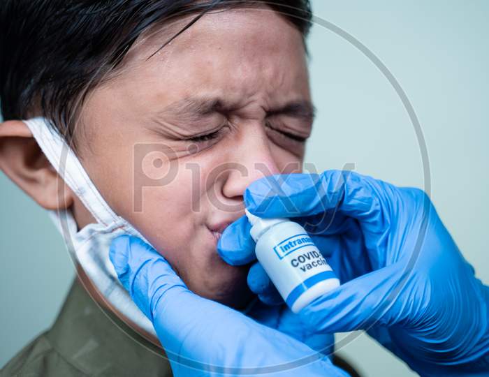 Head Shot Of Child With Medical Face Mask Getting Intranasal Coronvirus Covid-19 Vaccination Through Nostril From Doctor - Concept Of Covid Nasal Vaccine