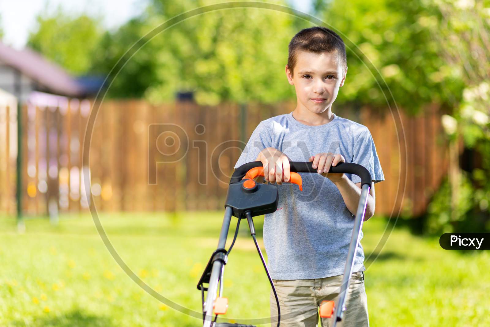Portrait A Boy  With An Electric Lawn Mower Mowing The Lawn.Beauty Boy  Pruning And Landscaping A Garden, Mowing Grass, Lawn, Paths.