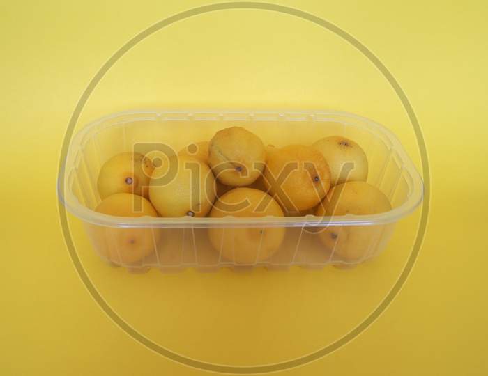 Lemon Fruits In Plastic Box Over Yellow Background