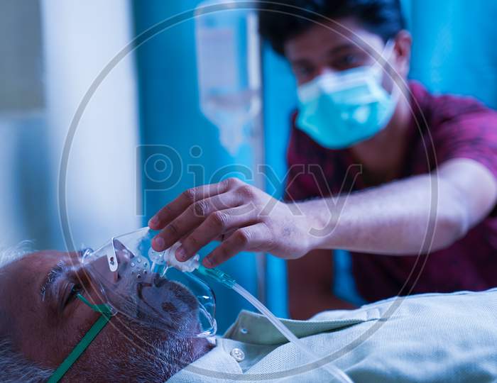 Son With Medical Face Mask Taking Care Of Sick Old Father At Hospital By Checking Ventilator Oxygen Mask - Concept Of Senior People Parental Health Care And Medical.