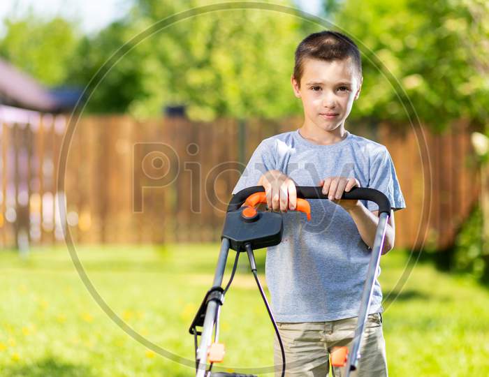 Portrait A Boy  With An Electric Lawn Mower Mowing The Lawn.Beauty Boy  Pruning And Landscaping A Garden, Mowing Grass, Lawn, Paths.