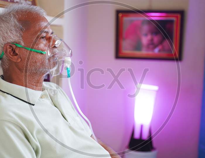 Old Man With Oxygen Concentrator Mask Reading News Using Mobile Phone During Home Isolation - Concept Of Low Oxygen Level Or Therapy Treatment From Home For Covid-19 Coronavirus Infected People