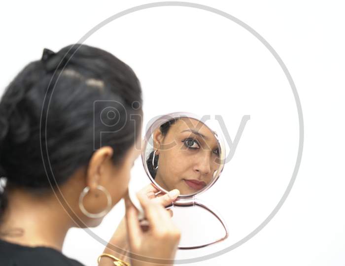 A Lady In 30S Putting Make Up In Front Of A Small Round Mirror
