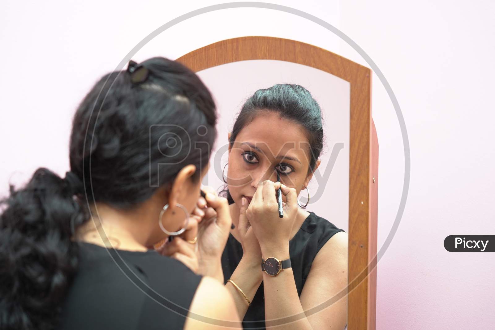 A Lady In 30S Putting Leye Liner Make Up In Front Of A Mirror.