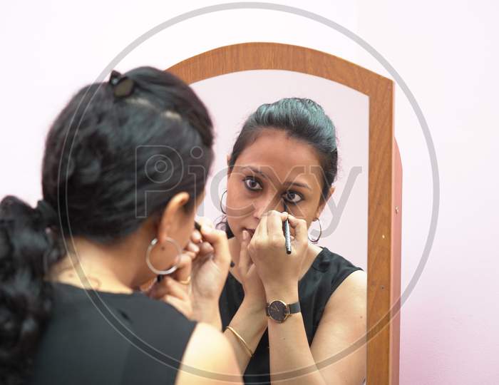 A Lady In 30S Putting Leye Liner Make Up In Front Of A Mirror.