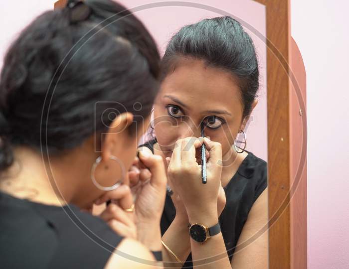 A Lady In 30S Putting Leye Liner Make Up In Front Of A Mirror. Close Up View
