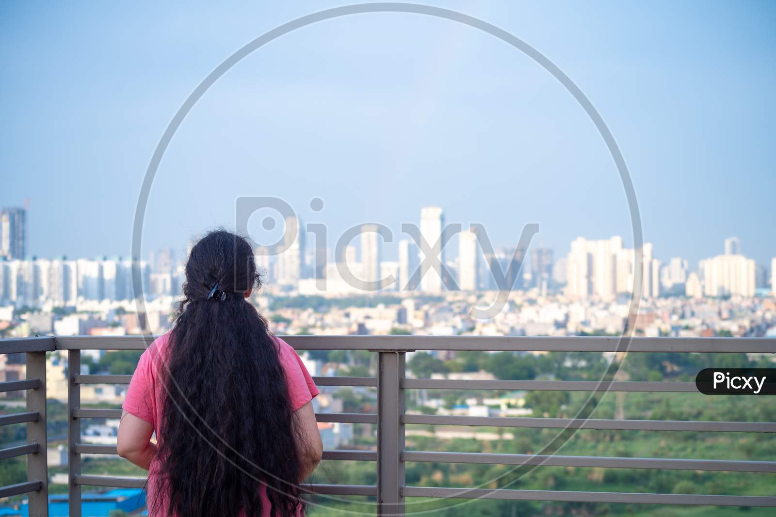 Zoomed In Shot Of Indian Woman With Long Hair In Front Of Huge Towers Skyscrapers Buildings With Offices Homes And Shopping Malls In Gurgaon Showing The Real Estate And Property While The Woman Looks Up In Amazement