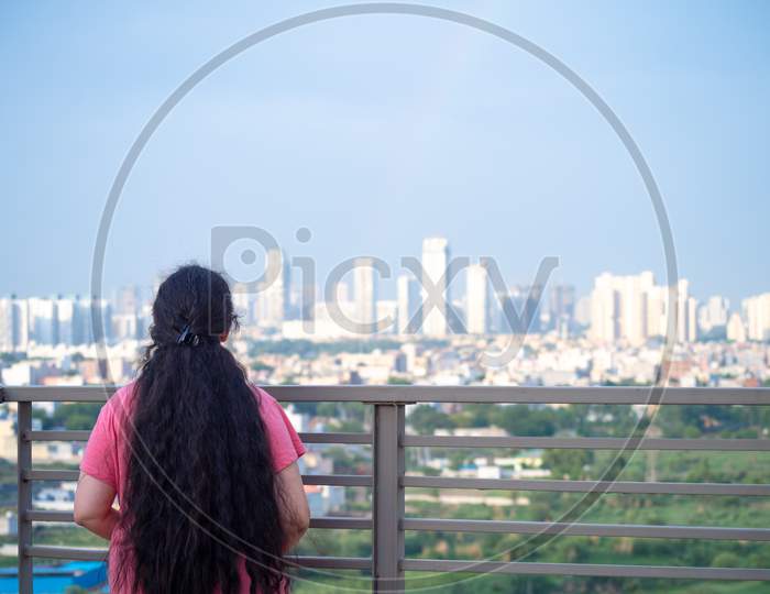 Zoomed In Shot Of Indian Woman With Long Hair In Front Of Huge Towers Skyscrapers Buildings With Offices Homes And Shopping Malls In Gurgaon Showing The Real Estate And Property While The Woman Looks Up In Amazement