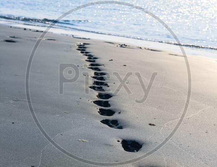 Footprints on the beach sand. Traces on the beach. Footsteps on the beach by the sea in summer. A man leaves footprints in the sand. Footprints in the sand.