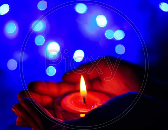 Burning candle in the hands of a girl with bokeh light. Christmas candles. Candlelight glowing in woman's hands. Praying, faith, religion concept.