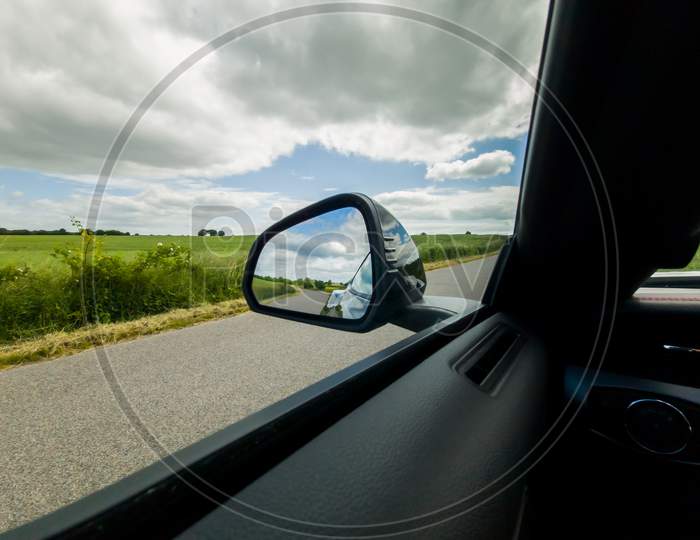 View Into The Side Mirror Of A Black Sports Car While Driving.