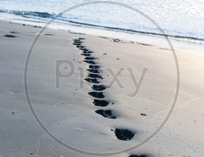 Footprints on the beach sand. Traces on the beach. Footsteps on the beach by the sea in summer. A man leaves footprints in the sand. Footprints in the sand.