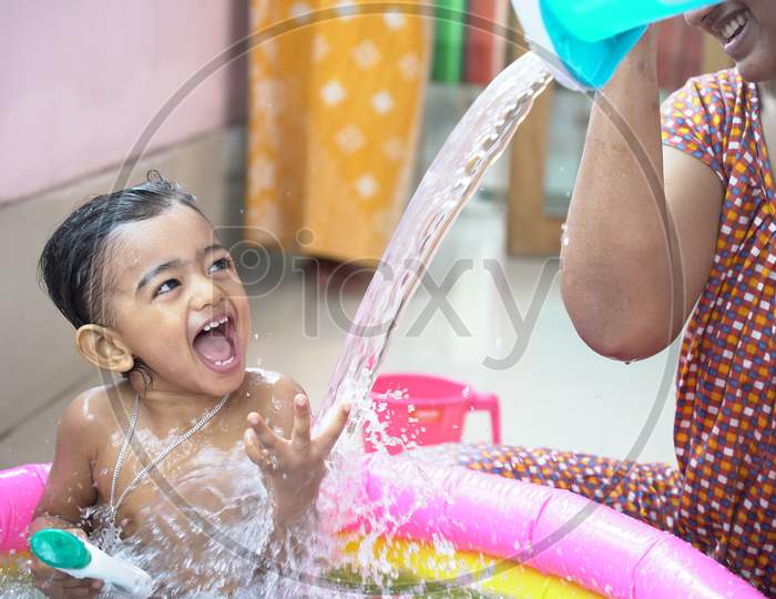 indian baby boy enjoying bath in an inflatable pool with water splashing and float toys.