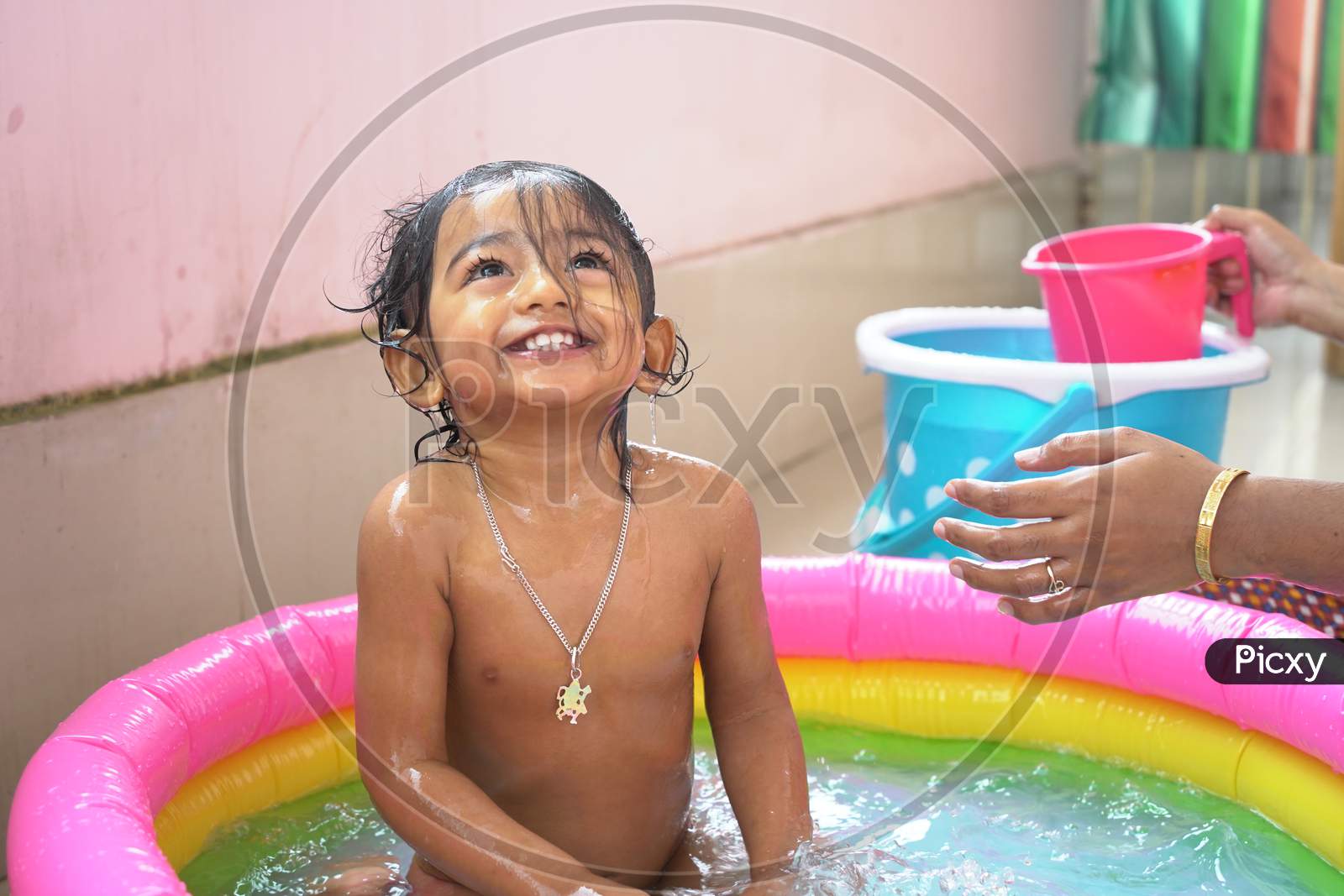 indian baby boy enjoying bath in an inflatable pool with water splashing and float toys.