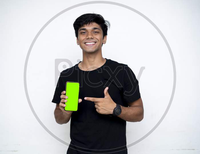 Young Indian Boy Holding A Mobile Phone And Point Towards It'S Screen. Mobile Phone With A Green Screen For Mockup.