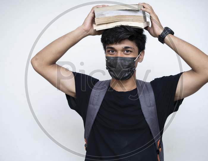 Young Indian Boy Holding Books On His Head, Wearing Mask, And Getting Ready For College After The Corona Virus Lockdown Is Over.