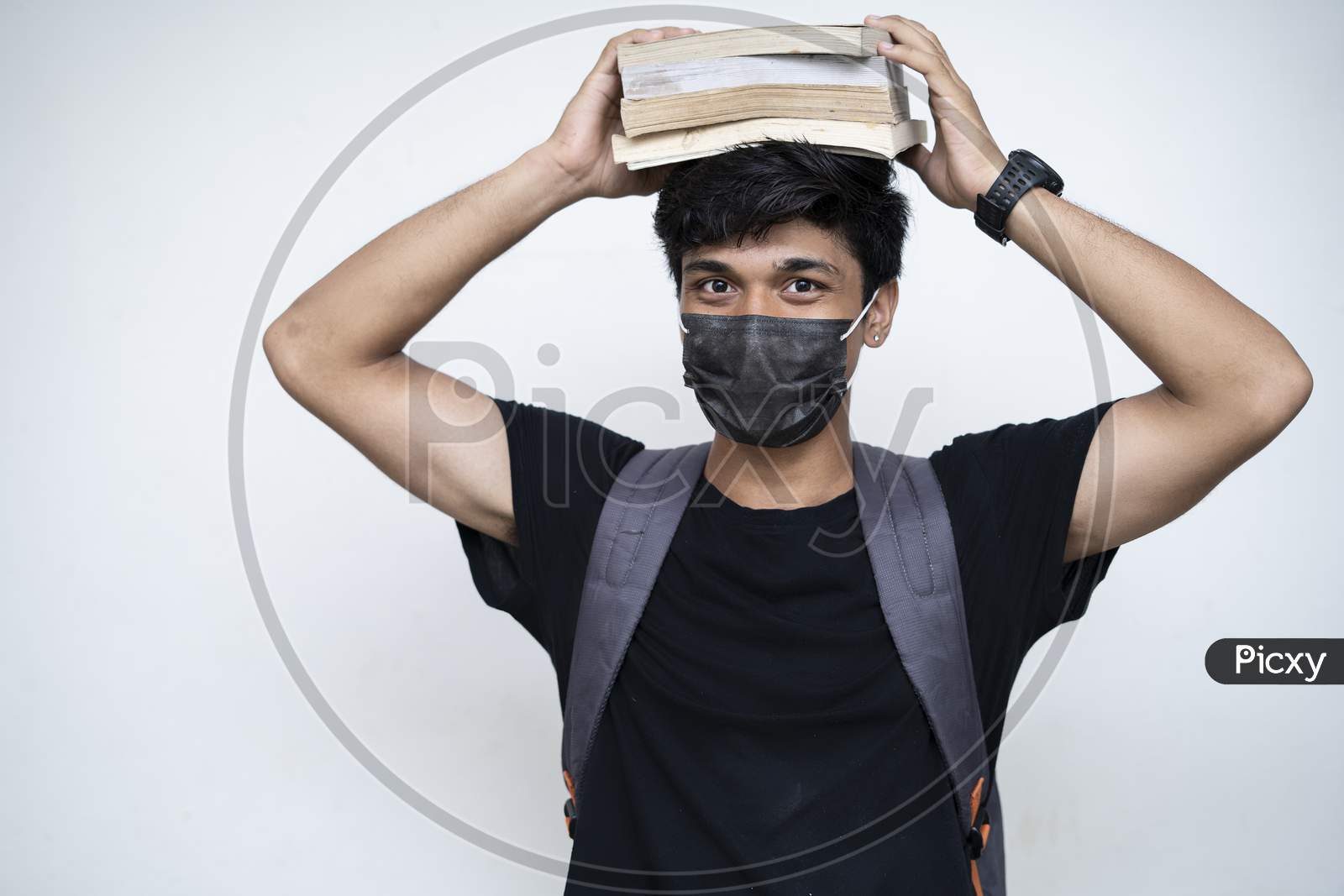 Young Indian Boy Holding Books On His Head, Wearing Mask, And Getting Ready For College After The Corona Virus Lockdown Is Over.