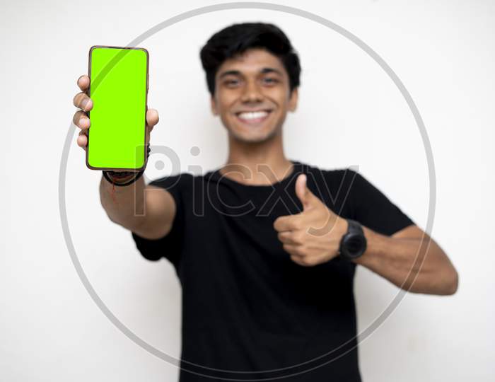 Young Indian Boy Holding A Mobile Phone And Point Towards It'S Screen. Mobile Phone With A Green Screen For Mockup.