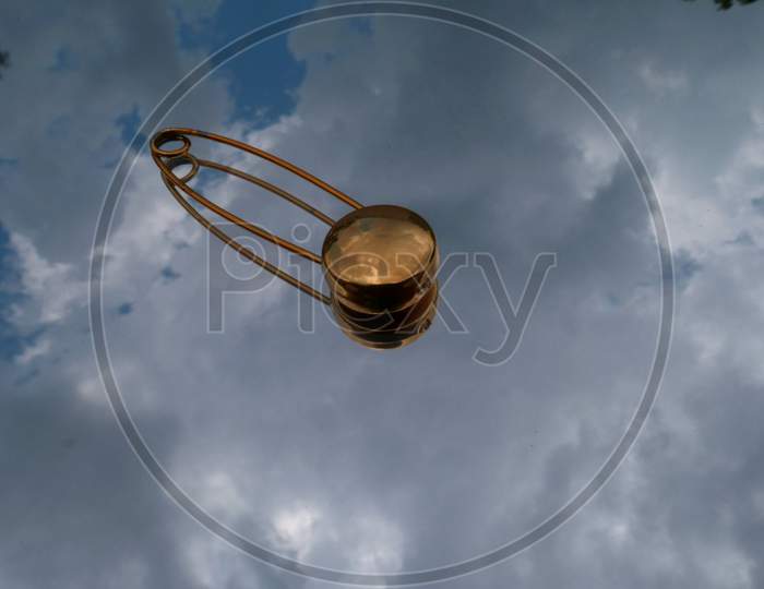 Golden Color Safety Pin Isolated On Sky Reflection Glass Surface.