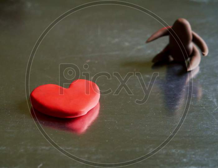 Red Color Heart Shape Clay With Blur Cartoon Men On Side Frame Presented For Loving Concept
