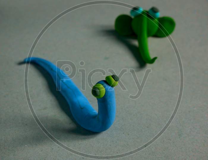 Clay Made Blue Color Snake Standing On Funny Posture With Blur Green Color Cartoon Elephant On Back