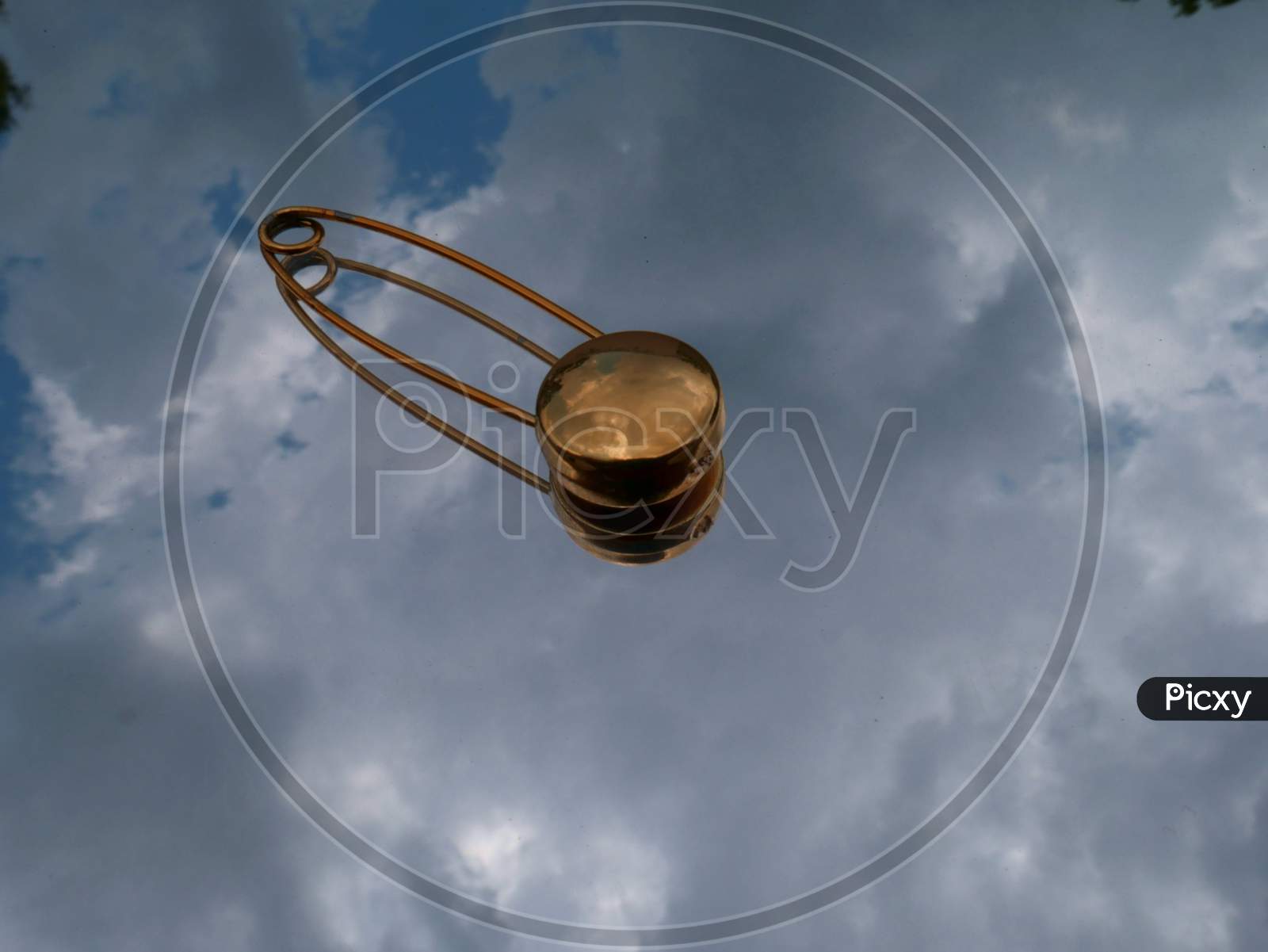 Golden Color Safety Pin Isolated On Sky Reflection Glass Surface.