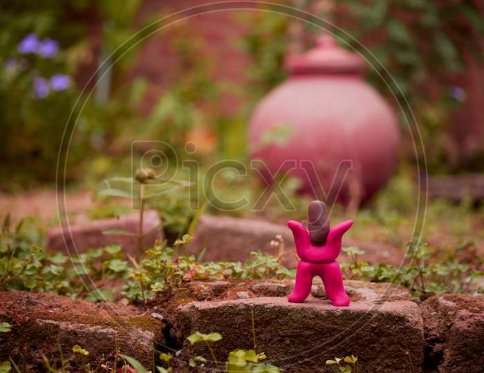 Red Color Cartoon Man Standing Upon Bricks Around Garden Made With Clay Art