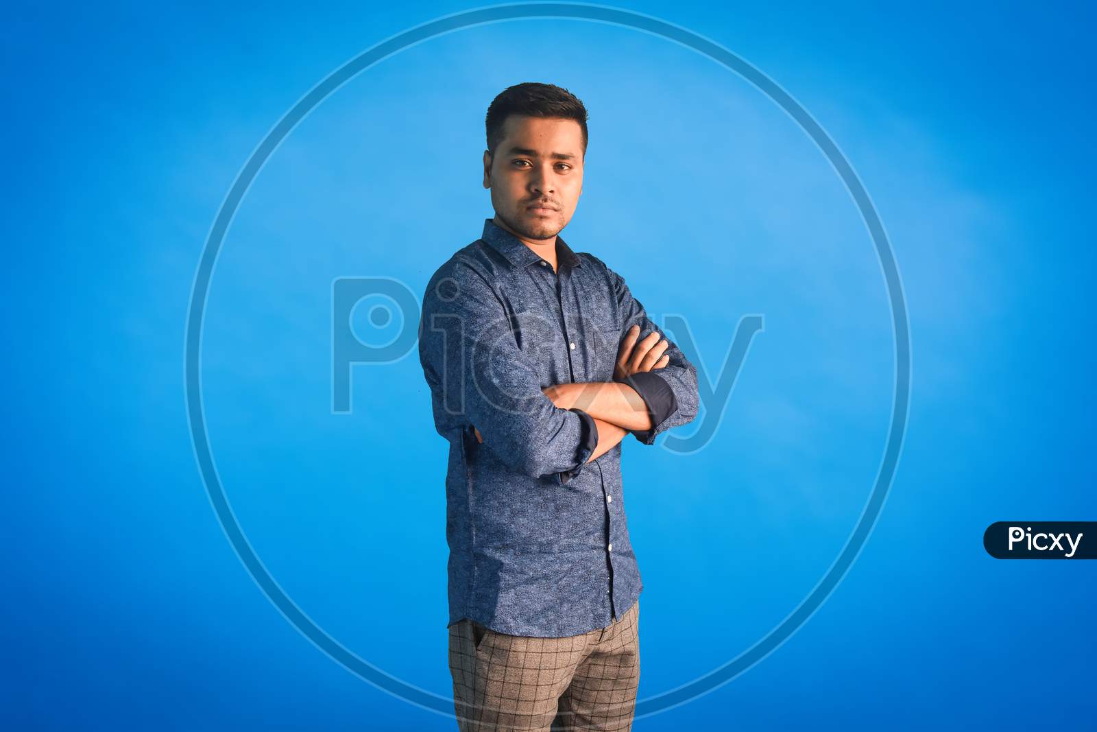 Portrait of serious Indian arm folded man standing on a blue background.