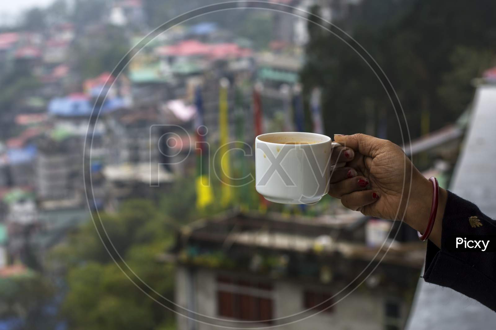 A Female Hand Enjoying Cup Of Tea With The View Of Gangtok City. Selective Focus.
