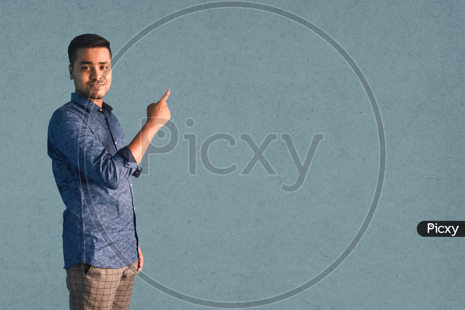 Young Indian man smiling and Pointing index finger aside in semi-casual clothes posing isolated on a grey background
