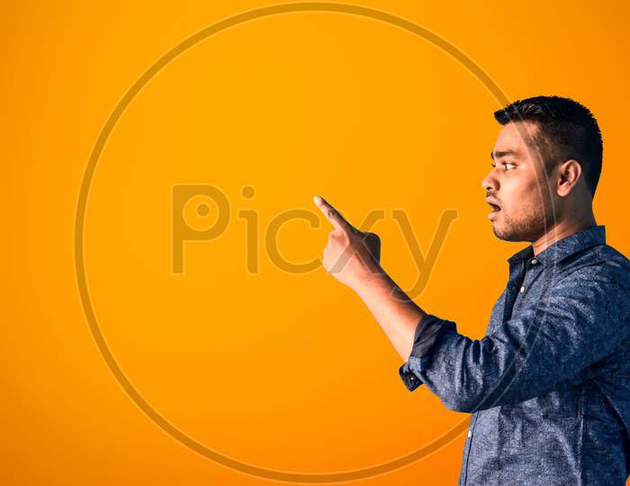A young Indian man in shock Pointing his index finger aside in semi-casual clothes posing isolated on an Orange background. Surprised young man. Brand endorsement concept.