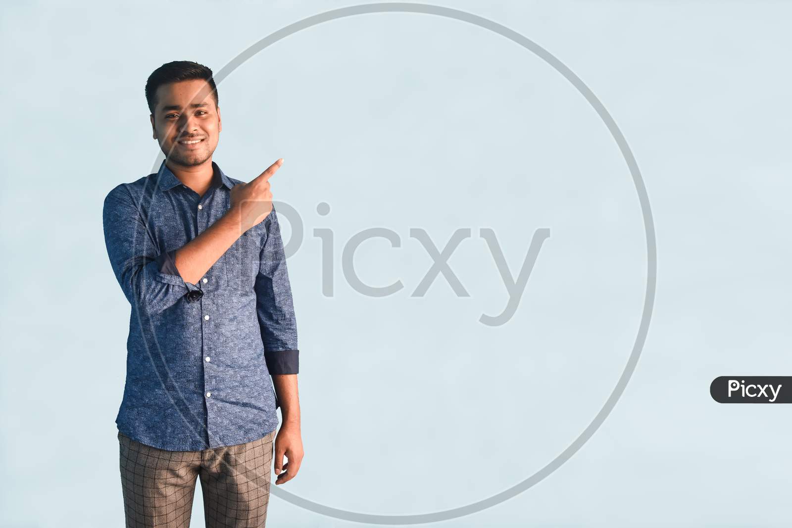 Young Indian man smiling and Pointing index finger aside in semi casual clothes posing isolated on a light blue background