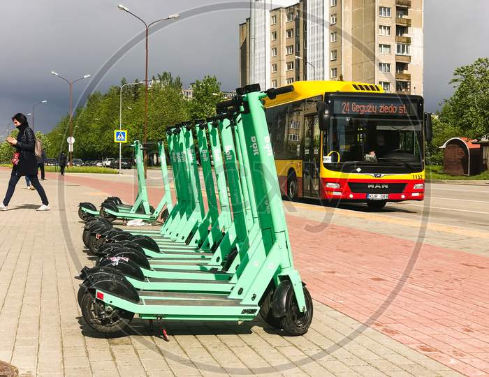 Siauliai, Lithuania - 29Th May, 2021: Gren Bol Electric Scooter Standing With Bus And Gil Walking In Background. Types Of Transportation In Lithuania And Baltics.
