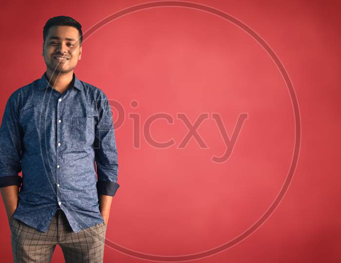 Young Indian businessman with a happy and cool smile on his face in semi-formal getup standing over isolated Red background Lucky person. Indian Business concept.