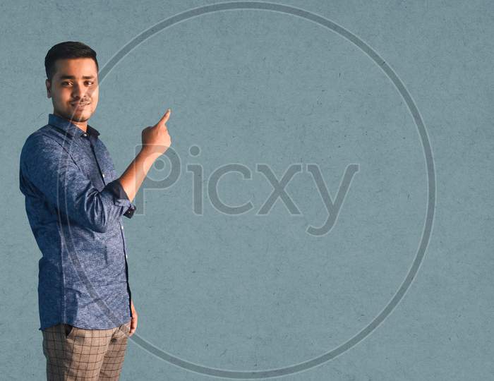 Young Indian man smiling and Pointing index finger aside in semi-casual clothes posing isolated on a grey background