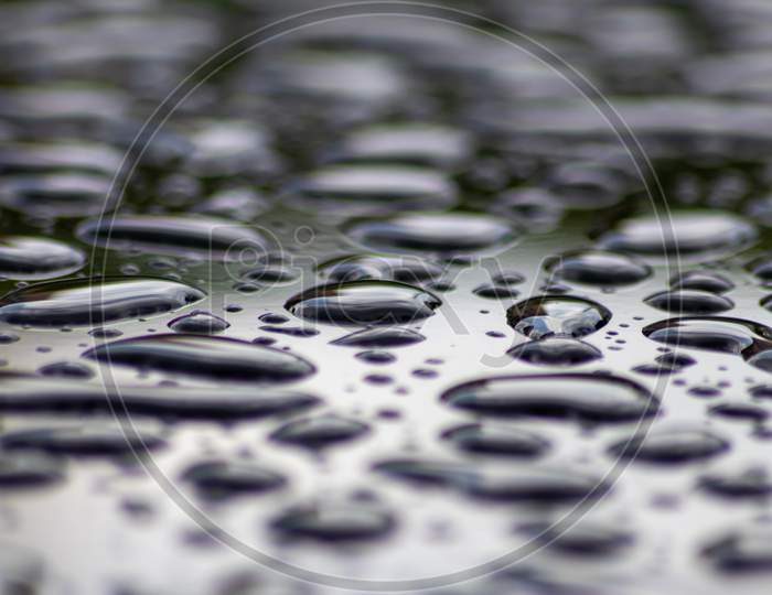 Beautiful raindrops on wet surface of a car metallic shiny bubbles and zen meditation freshness on rainy day with droplets and blurred background as selective focus as fluid background clear water