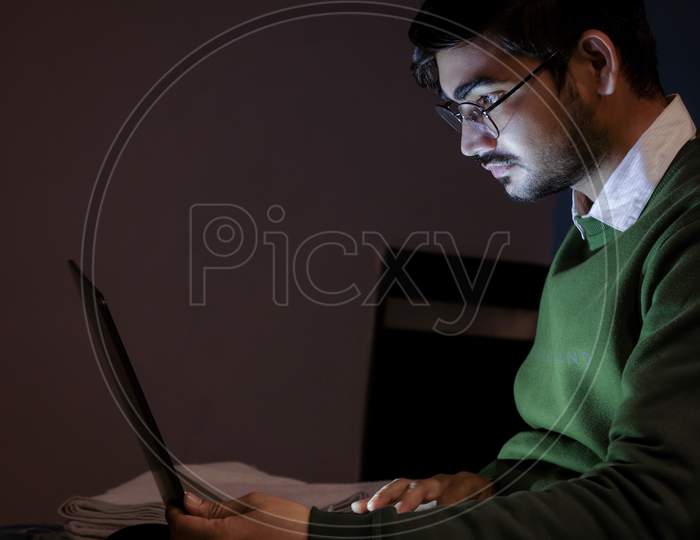 A young handsome indian boy working on laptop.