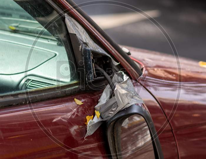 Broken side mirror hanging at a demolished car after car accident or vandalism injury and insurance loss due to hit and run shows dangerous traffic in cities and the need for car insurance for safety