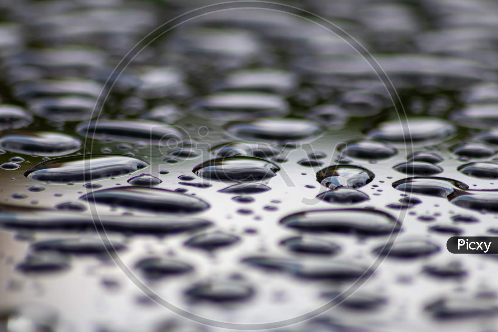 Beautiful raindrops on wet surface of a car metallic shiny bubbles and zen meditation freshness on rainy day with droplets and blurred background as selective focus as fluid background clear water