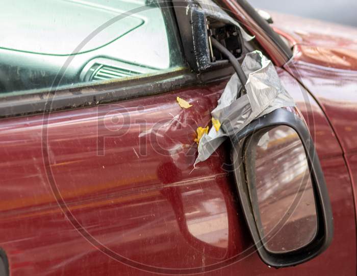 Broken side mirror hanging at a demolished car after car accident or vandalism injury and insurance loss due to hit and run shows dangerous traffic in cities and the need for car insurance for safety