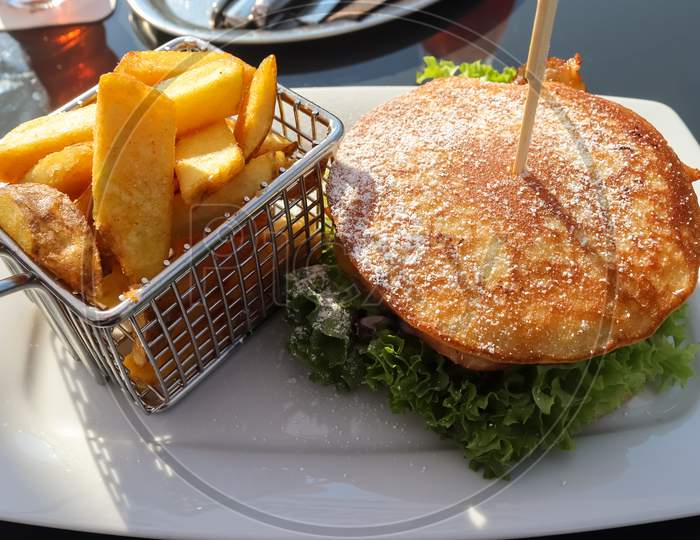 A Grilled Burger With Salad On A Plate With French Fries.