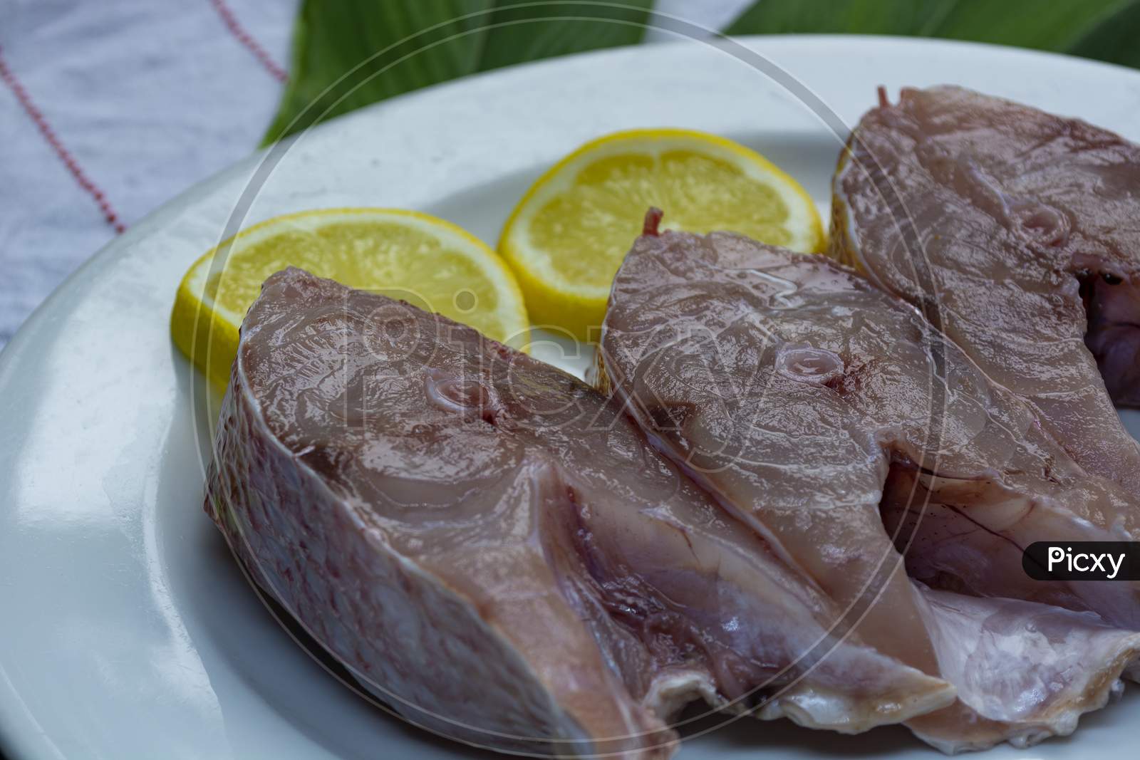 Fresh Raw Fish On White Plate With Green Leaf And Lemon