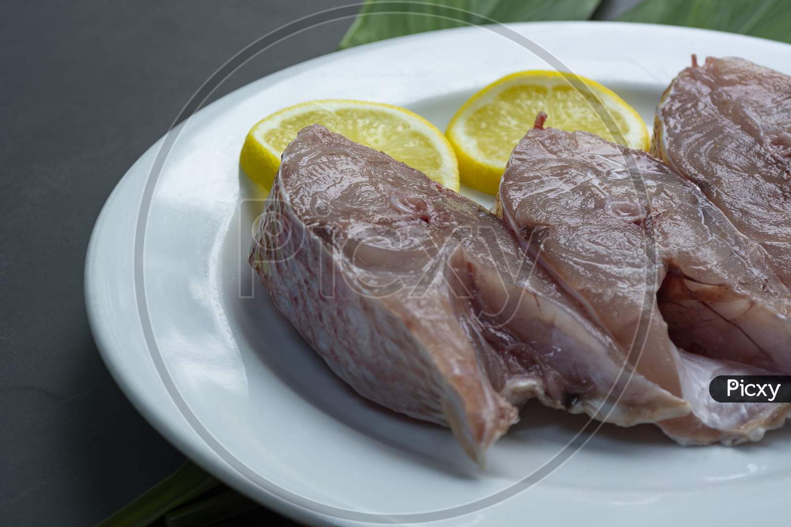 Fresh Raw Fish On White Plate With Green Leaf And Lemon