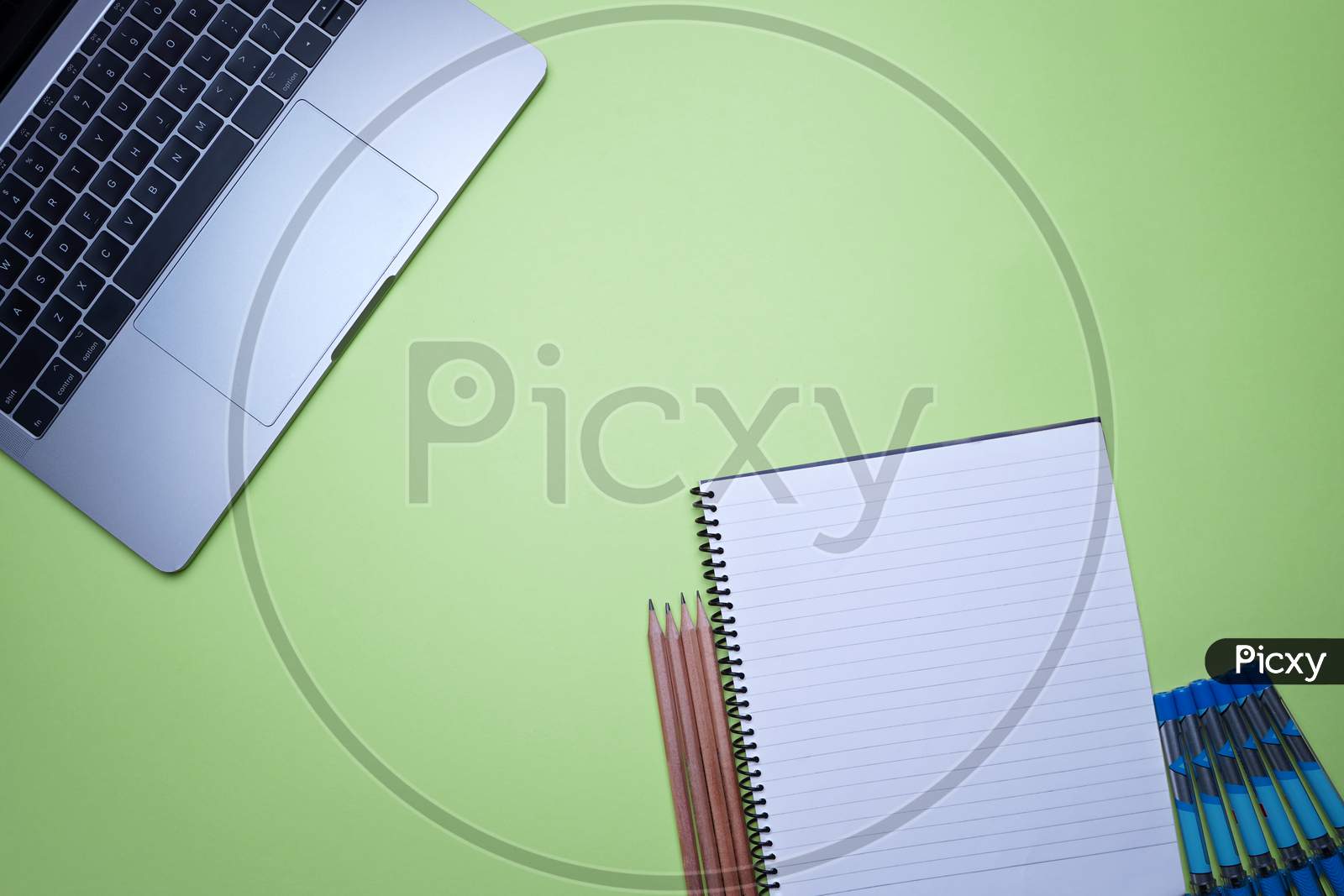 Table Top Flat Lay Of Office. Top View Laptop, Spiral Notebook And Pencils On A Green Background