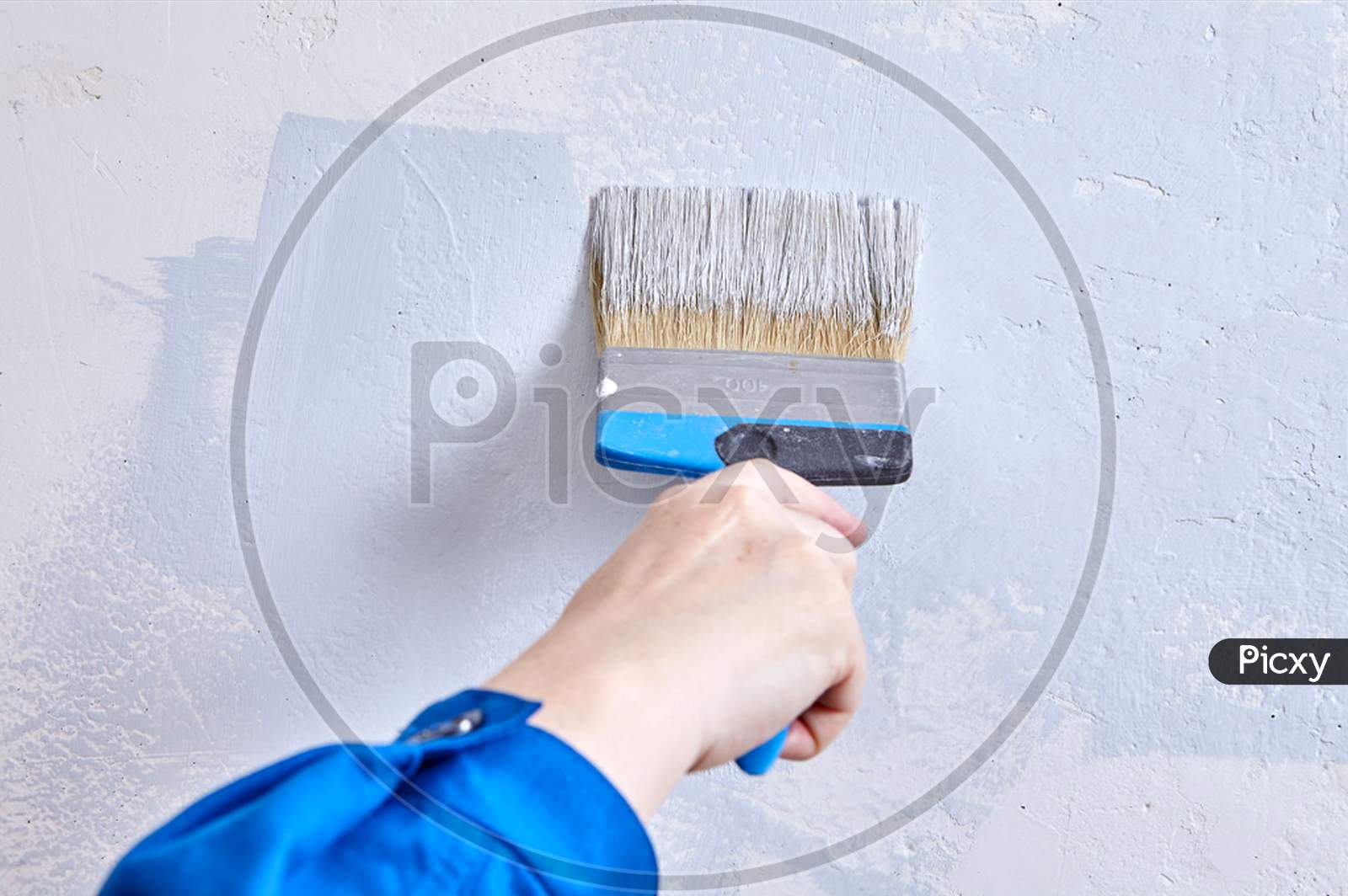 Painter Paints The Wall With A Paintbrush. Handyman Is Covering Beton With Color Using Paint Brush During Renovation.