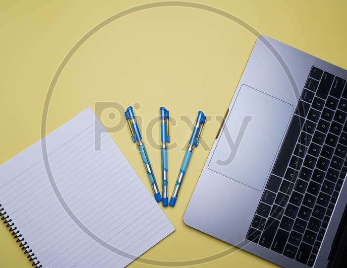 Creative Office, Business Professional Table Top, Flat Lay. Laptop, Pen And White Spiral Notebook On Yellow Background