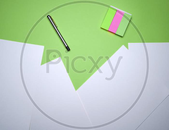 Creative Flat Lay, Table Top, Top View Of Business Office, Student Workspace, Homework. White Paper Sheet, Pen And Sticky Notes On Green Background