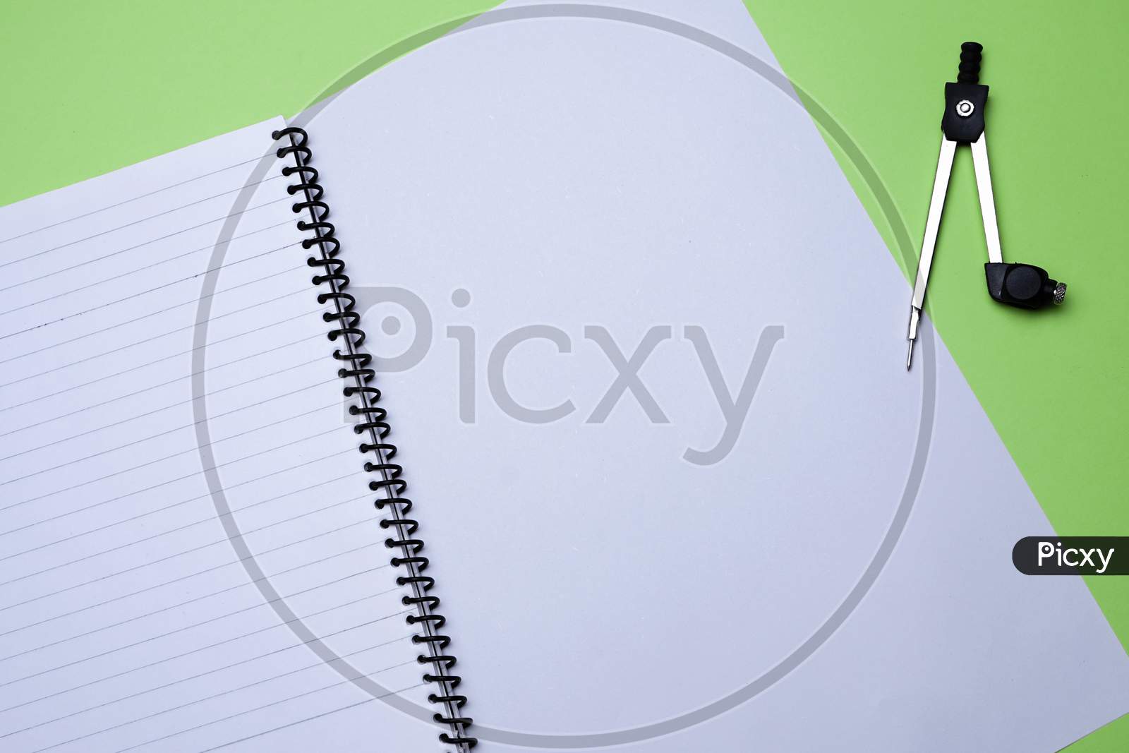 Creative Flat Lay, Table Top, Overview For Students Homework, Education, Office And Business.Spiral Notebook, White Sheet And Compass On Green Background